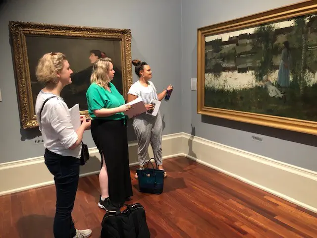 Three museum visitors viewing framed paintings
