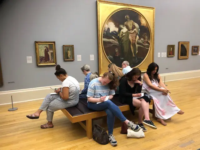 Visitors sketching on bench in art gallery